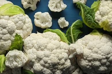 Fresh whole and cut cauliflowers on blue wooden table, top view