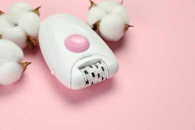 Photo of Modern epilator near fluffy cotton flowers on pink background, closeup. Space for text