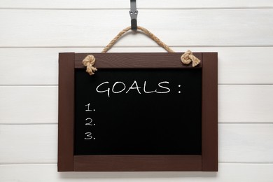 Image of Blackboard with word GOALS and empty checklist on hanging on white wooden background