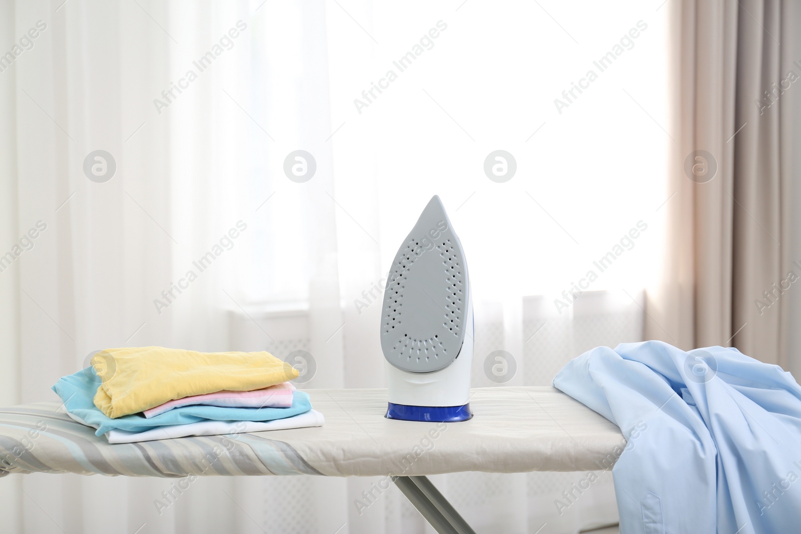 Photo of Board with modern iron and clean clothes indoors. Laundry day