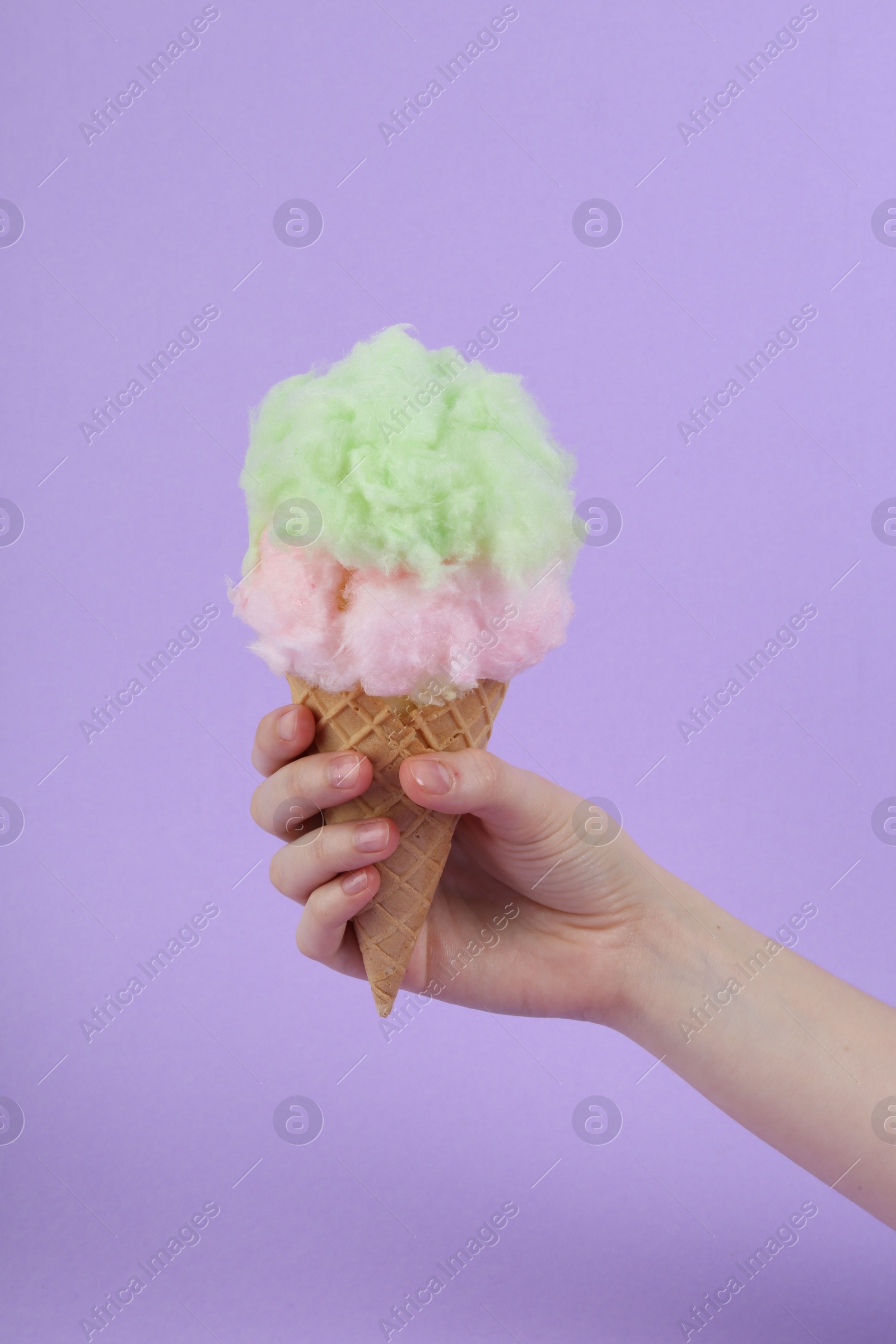 Photo of Woman holding waffle cone with cotton candy on violet background, closeup