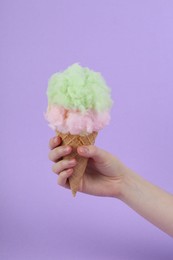 Woman holding waffle cone with cotton candy on violet background, closeup