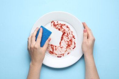 Photo of Woman washing dirty plate with sponge on light blue background, top view