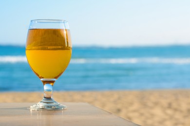Photo of Glass of cold beer on wooden table at beach. Space for text