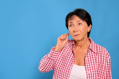 Photo of Senior woman cleaning ear with cotton swab on light blue background. Space for text