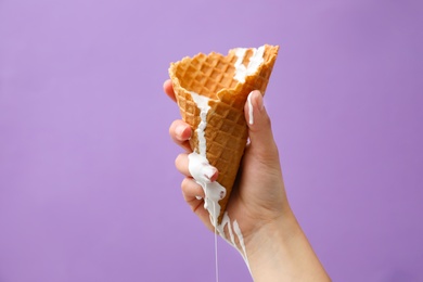 Photo of Woman holding wafer cone with molten ice cream on violet background, closeup
