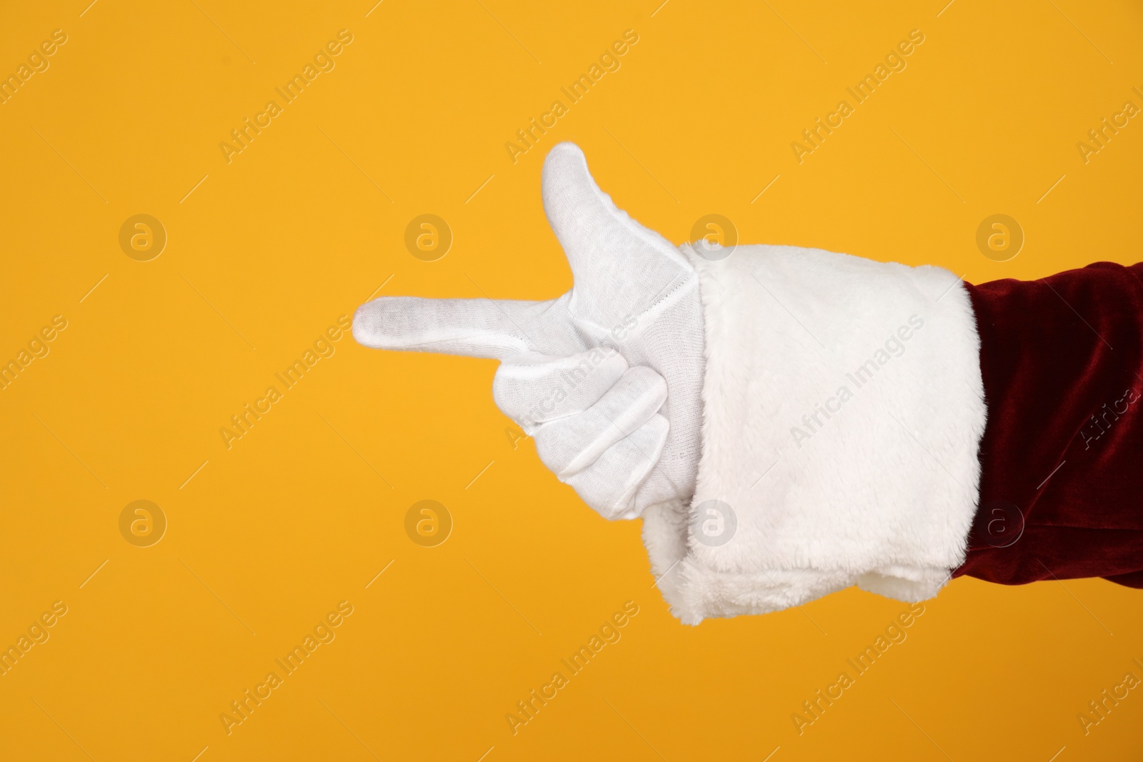 Photo of Santa Claus pointing at something on yellow background, closeup of hand