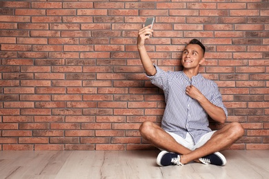 Photo of Young man taking selfie against brick wall. Space for text