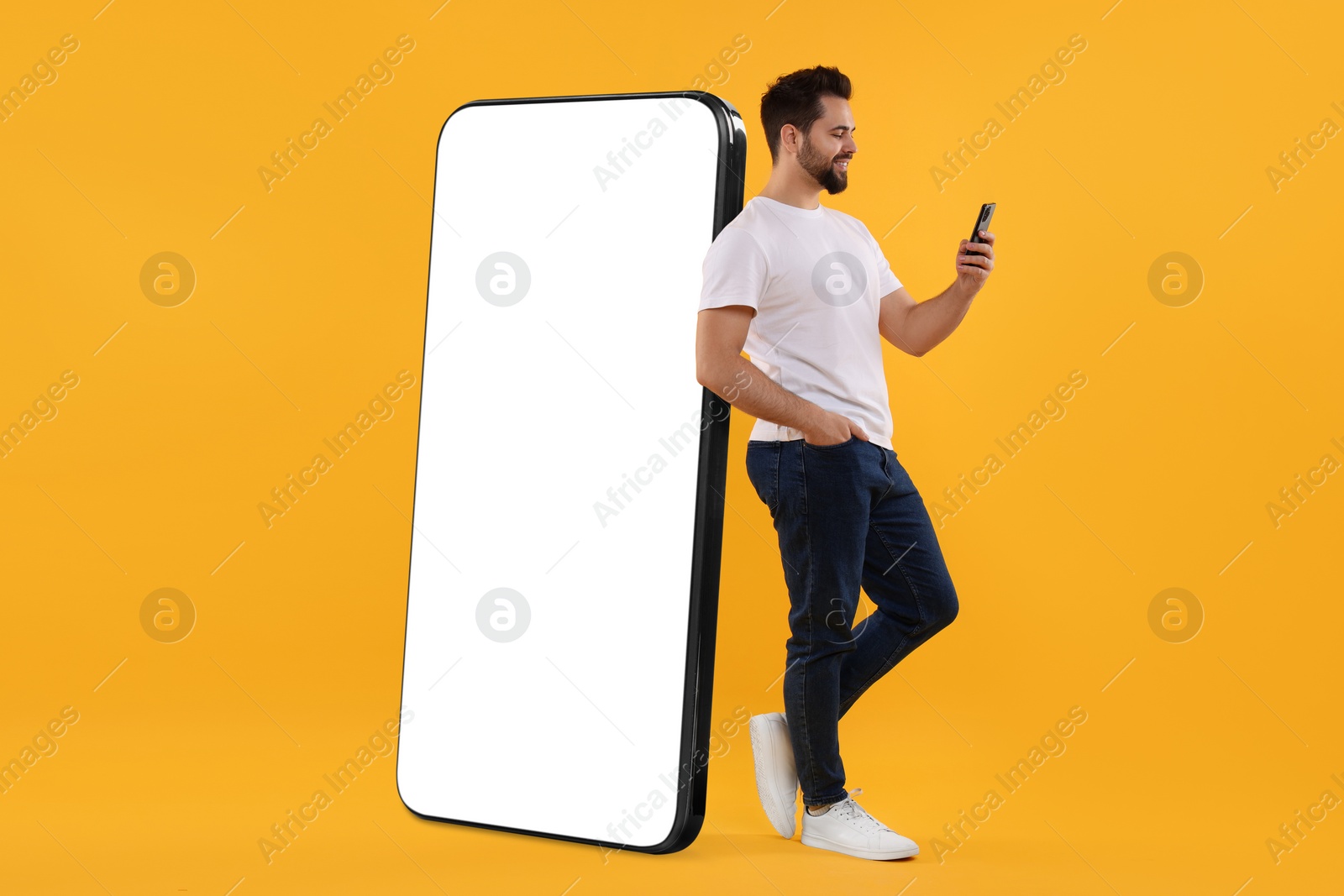 Image of Man with mobile phone standing near huge device with empty screen on dark beige background. Mockup for design