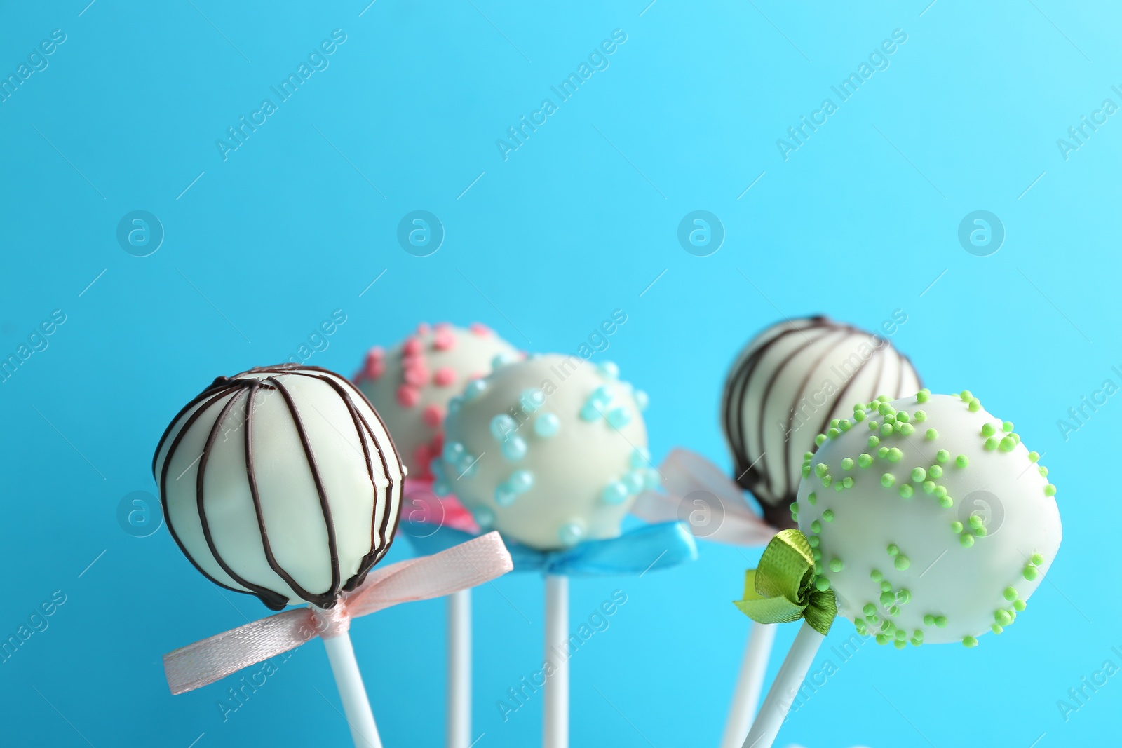 Photo of Tasty cake pops with bows on light blue background