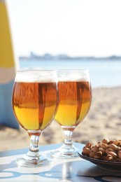Photo of Glasses of cold beer and pistachios on table near sea