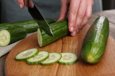 Woman cutting cucumber on wooden board at table, closeup