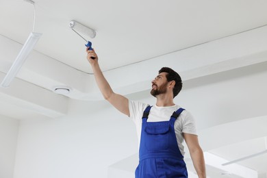 Photo of Handyman with roller painting ceiling in room, low angle view