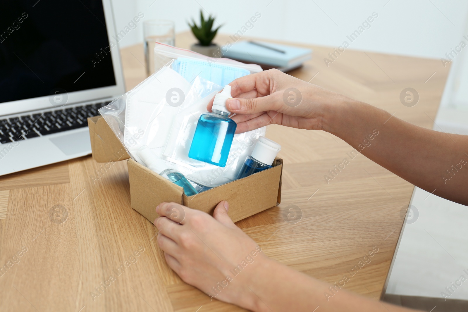 Photo of Woman unpacking box with antiseptics and respiratory masks at wooden table, closeup. Protective essentials during COVID-19 pandemic