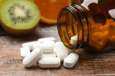 Photo of Dietary supplements. Overturned bottle, pills and fruits on wooden table, closeup