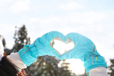 Photo of Young woman making heart with hands outdoors, closeup. Winter vacation