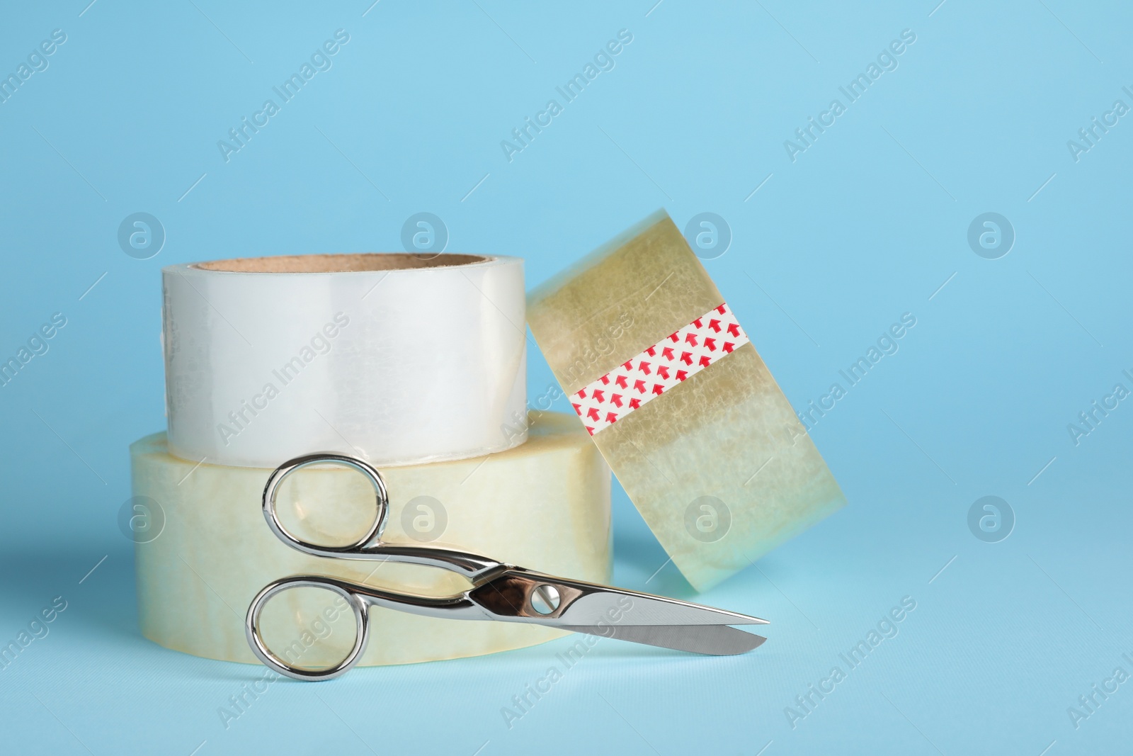 Photo of Rolls of adhesive tape and scissors on light blue background. Space for text