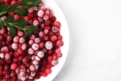 Photo of Frozen red cranberries and green leaves on white table, top view. Space for text