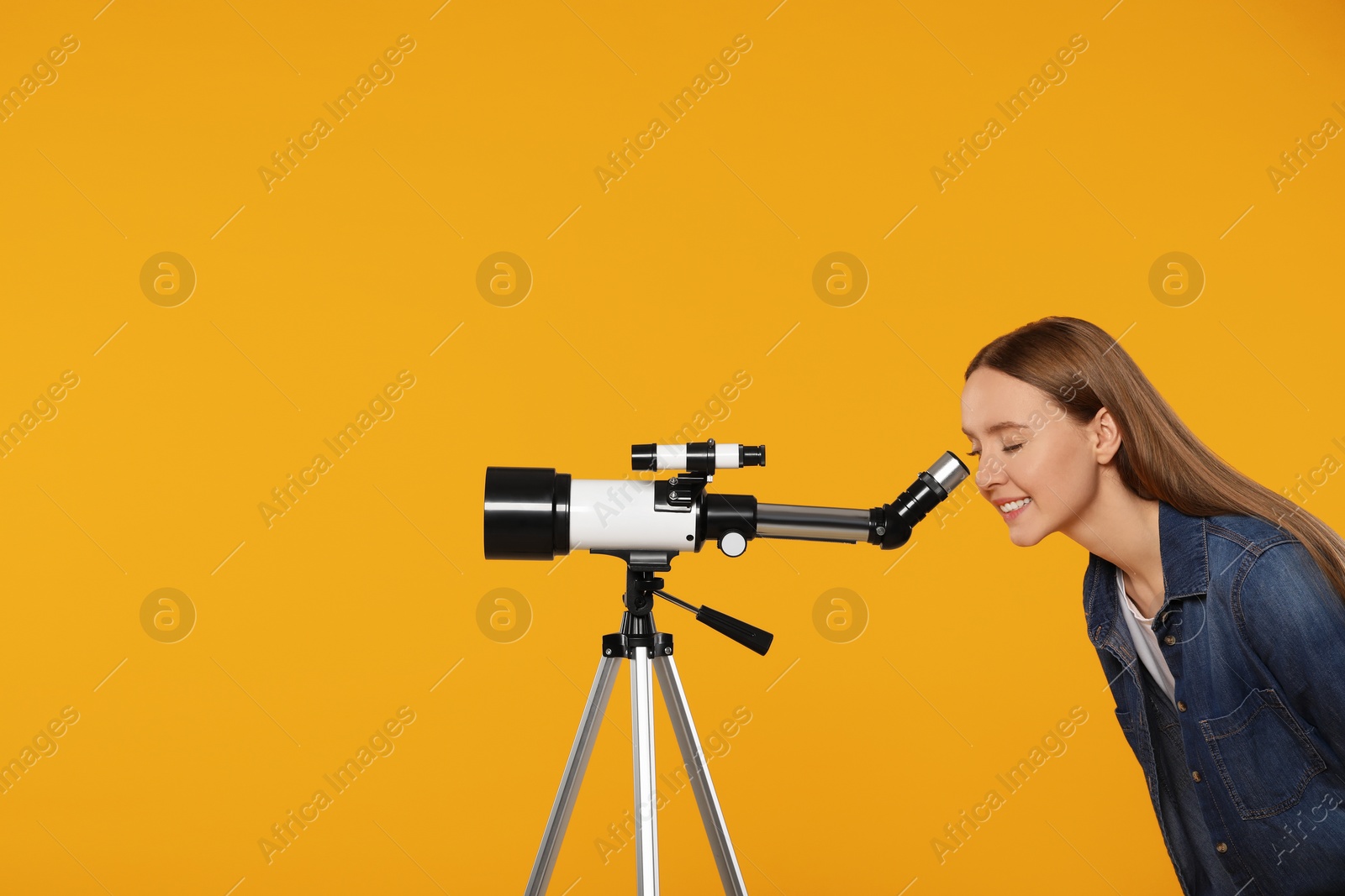 Photo of Young astronomer looking at stars through telescope on orange background, space for text