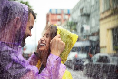 Image of Young couple in raincoats enjoying time together on city street, space for text