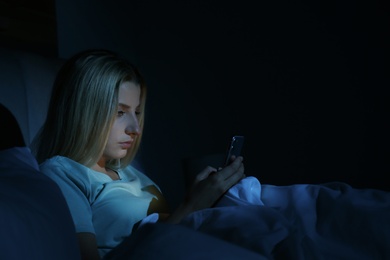 Photo of Young woman using smartphone in bed at night. Nomophobia and sleeping disorder problem