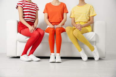 Women wearing bright tights sitting on sofa indoors, closeup