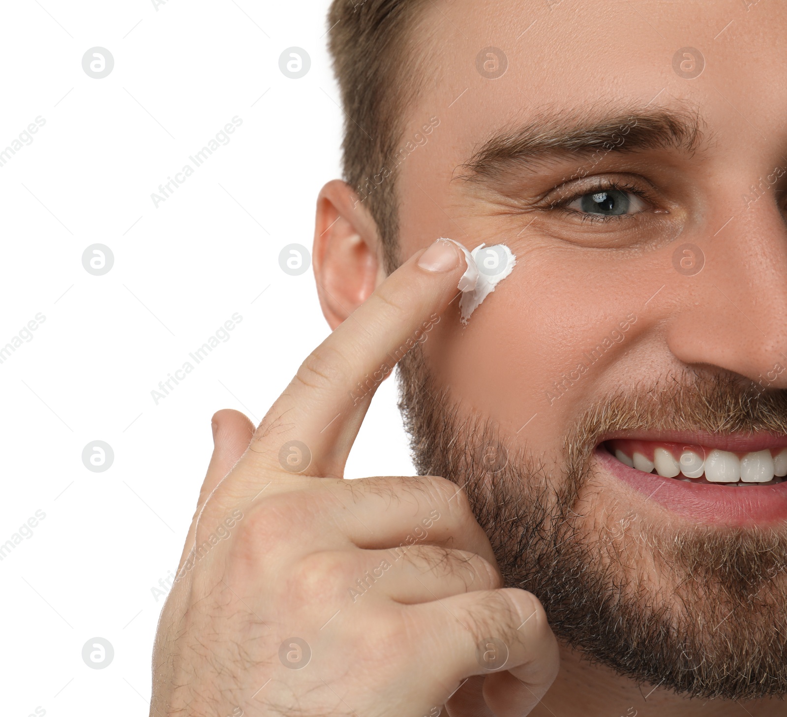 Photo of Happy young man applying facial cream on white background, closeup