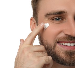 Happy young man applying facial cream on white background, closeup