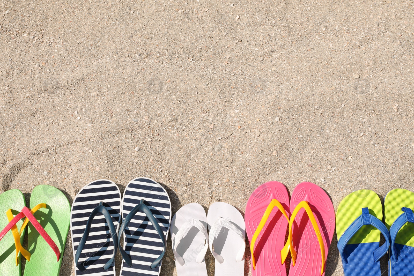 Photo of Many different flip flops on sand, flat lay. Space for text