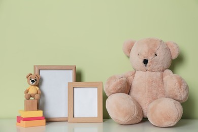 Photo of Empty photo frames, toy bears and building blocks on white table near light green wall. Space for design