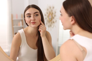 Photo of Young woman with skin problem looking at mirror indoors