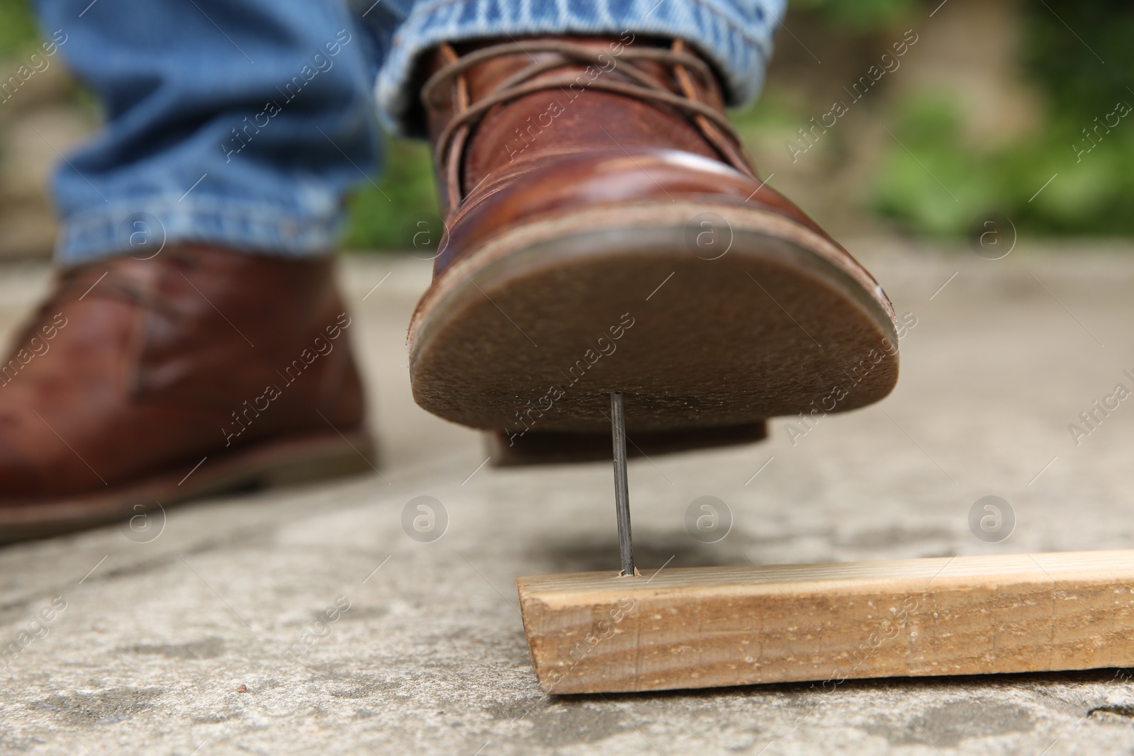 Photo of Careless man stepping on nail in wooden plank outdoors, closeup