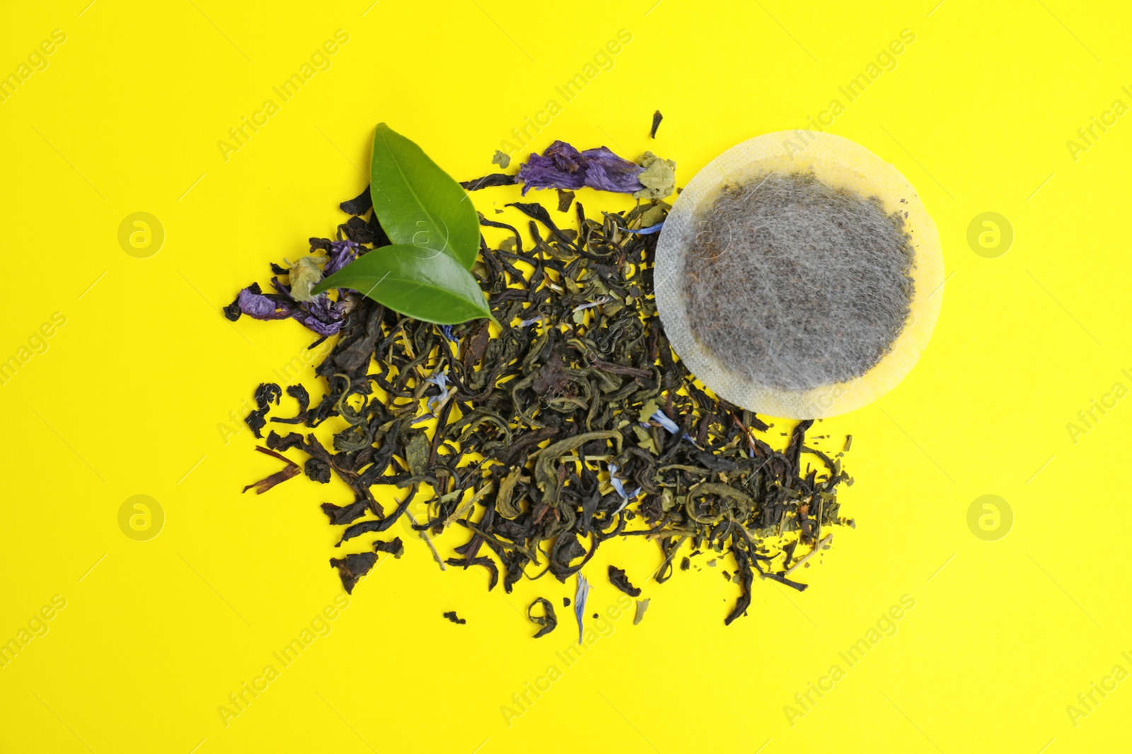 Photo of Tea bag with scattered dry leaves on color background, top view