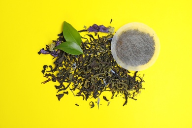 Photo of Tea bag with scattered dry leaves on color background, top view