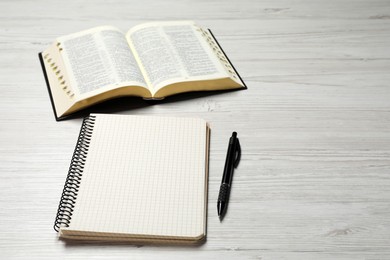 Open Bible, empty notebook and pen on white wooden table, space for text. Christian religious book