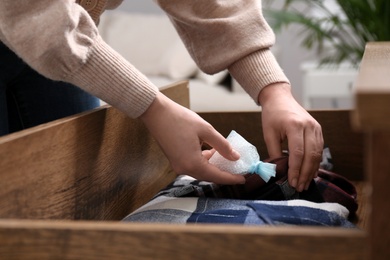 Photo of Woman putting scented sachet into drawer with clothes, closeup