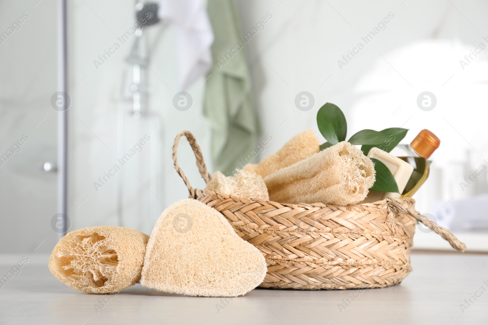 Photo of Natural loofah sponges near wicker basket on table in bathroom