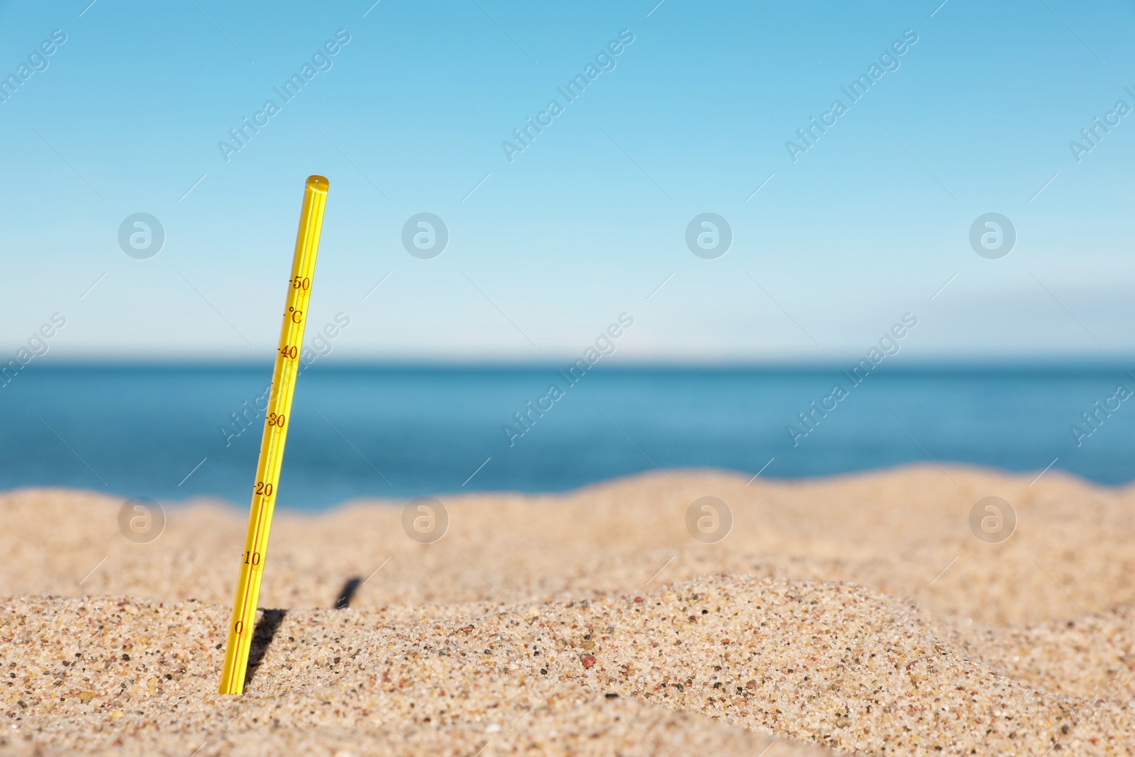 Photo of Yellow weather thermometer in sand near sea, space for text