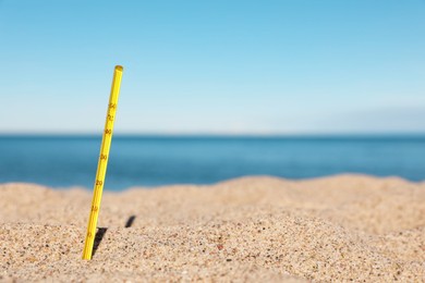 Yellow weather thermometer in sand near sea, space for text