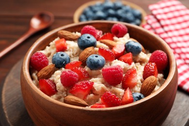 Photo of Tasty oatmeal porridge with berries and almond nuts in bowl served on table, closeup