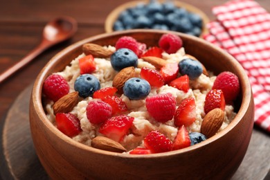 Tasty oatmeal porridge with berries and almond nuts in bowl served on table, closeup