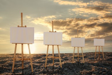 Image of Wooden easels with blank canvases on beach near sea at sunrise 