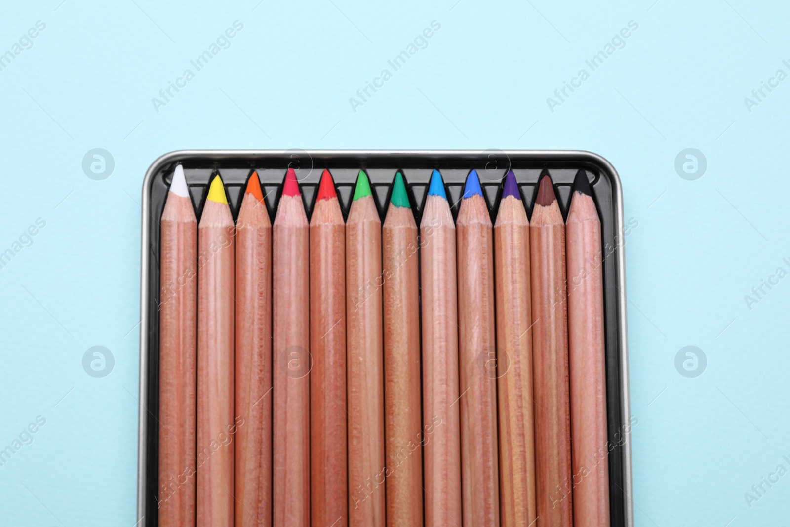Photo of Colorful pastel pencils in box on light blue background, top view. Drawing supplies