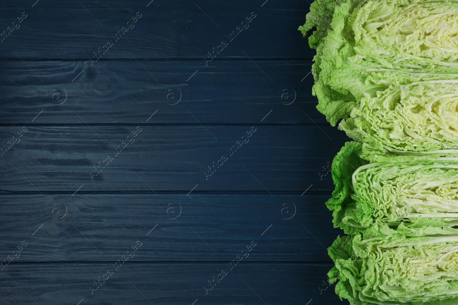 Photo of Cut fresh ripe Chinese cabbages on blue wooden table, flat lay. Space for text