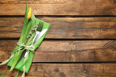 Photo of Cutlery set and floral decor on wooden table, top view with space for text. Easter celebration