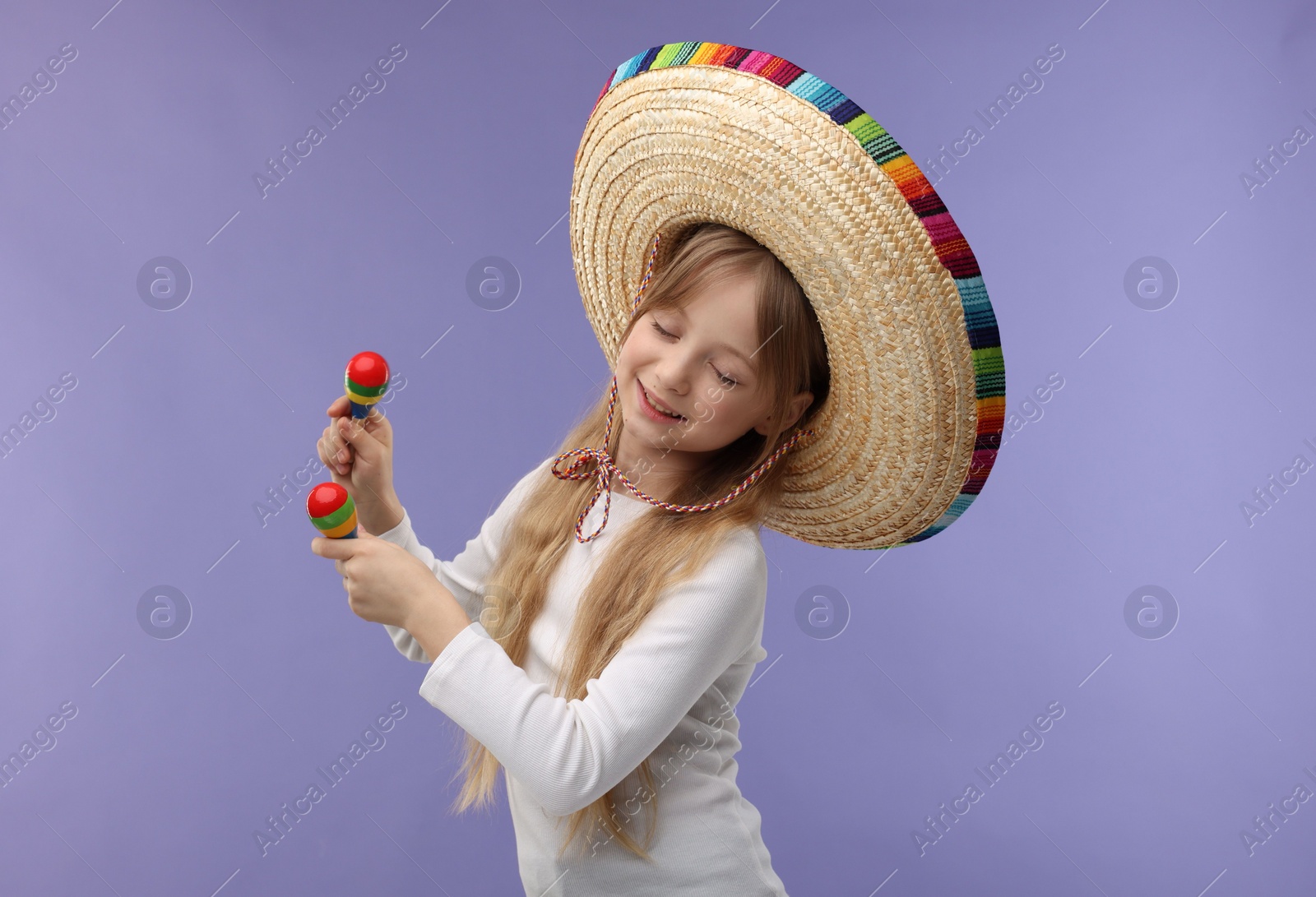 Photo of Cute girl in Mexican sombrero hat dancing with maracas on purple background