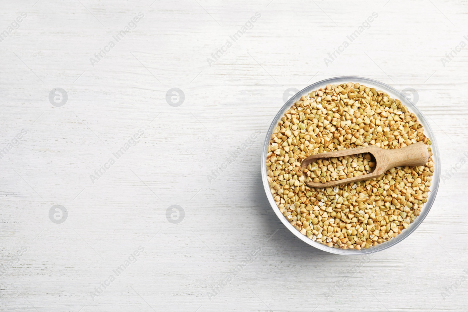 Photo of Uncooked green buckwheat grains in bowl on white wooden table, top view. Space for text