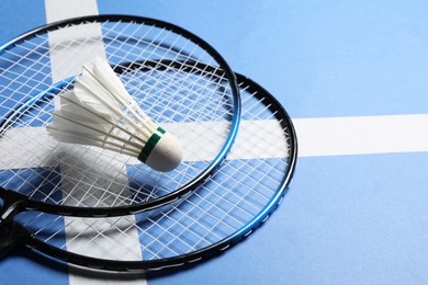 Feather badminton shuttlecock and rackets on blue background, closeup. Space for text