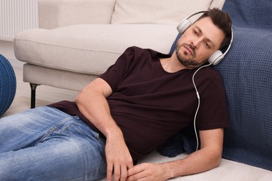 Upset man listening to music through headphones while lying on floor at home. Loneliness concept