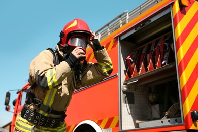 Firefighter in uniform wearing helmet and mask near fire truck outdoors, low angle view